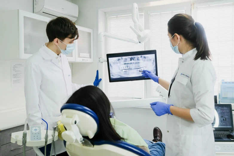 two women standing in a dental office with one getting the teeth brushed