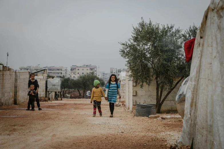 a group of young children walk across a dirt road