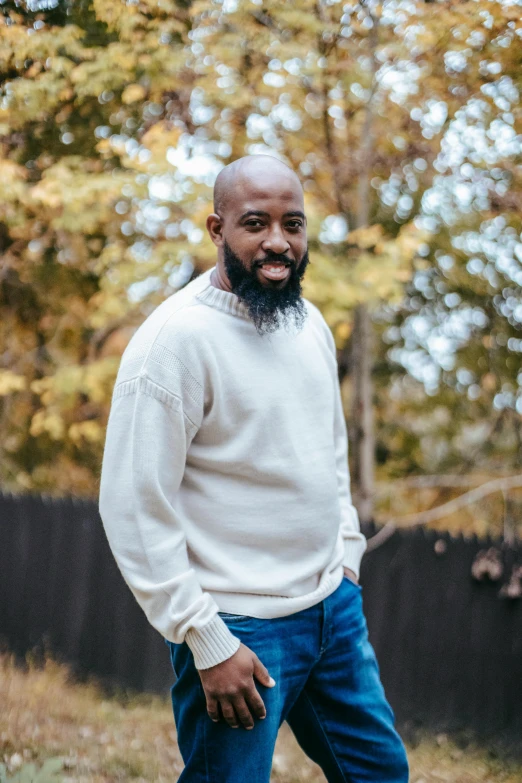 man with goatee wearing sweater and jeans in front of trees