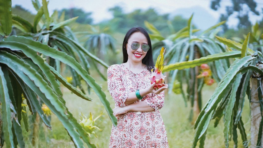 a woman in a dress smiles holding leaves and flower