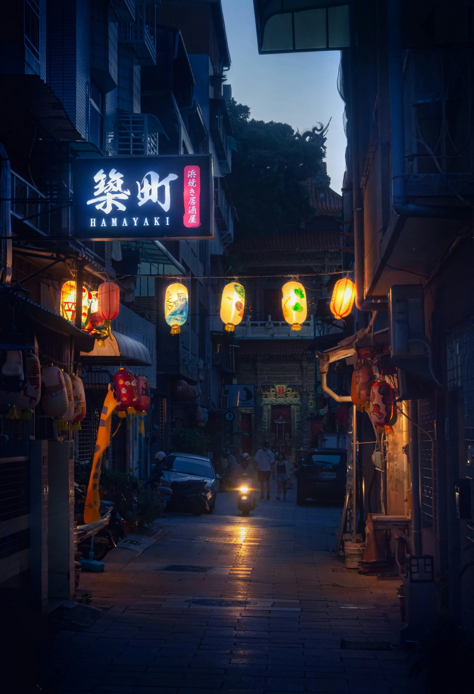 a narrow road with a person walking on it in the middle of the night