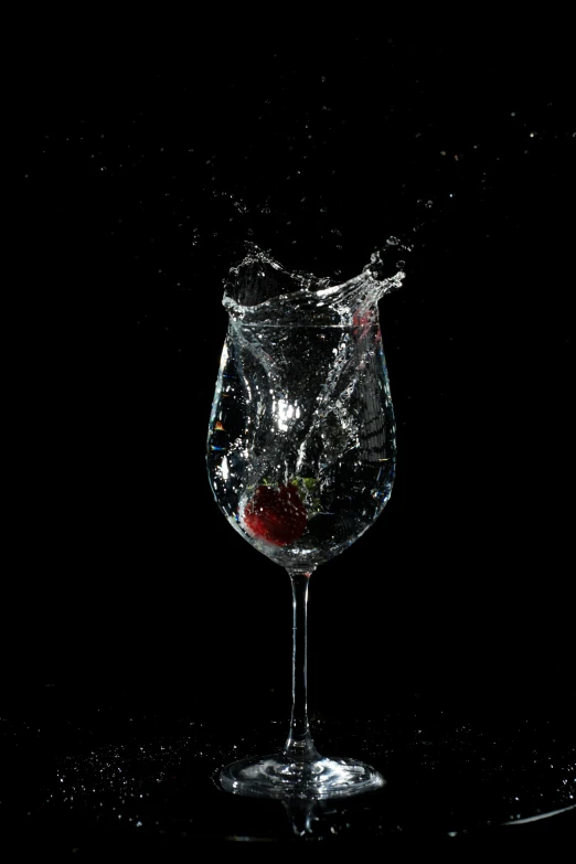 a wine glass with water, some splashing and a red apple
