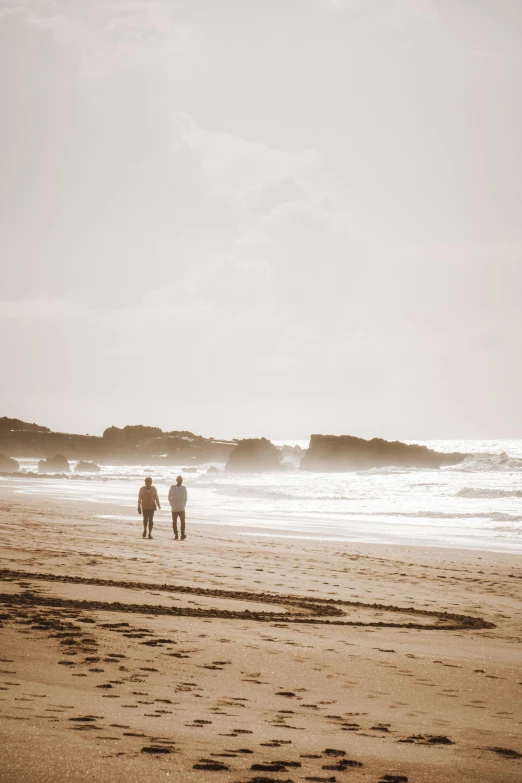 two men walking on a beach towards the ocean