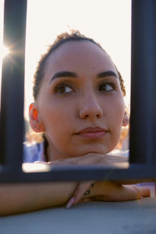 the woman stares out through a metal fence