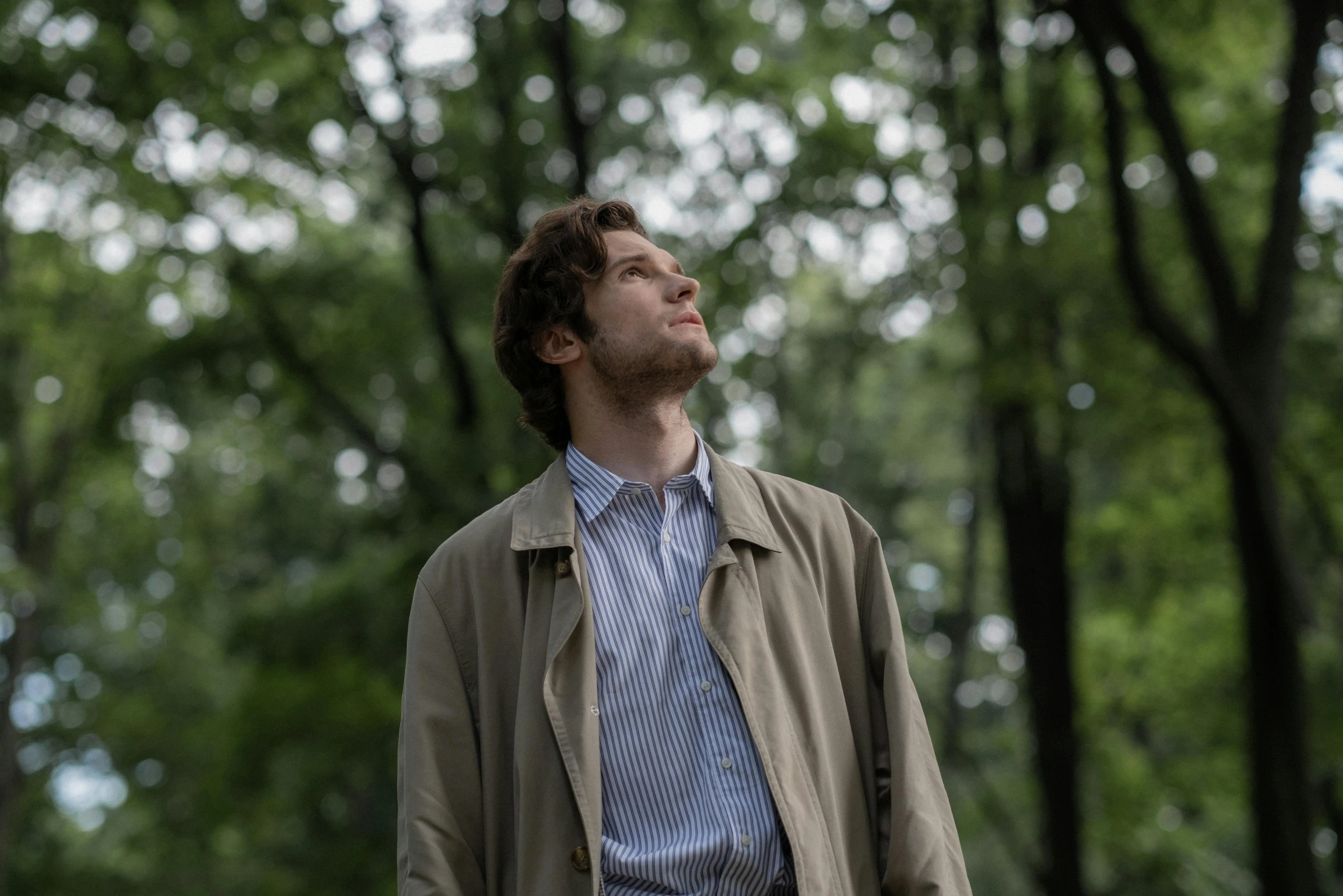 man standing near trees in jacket and tie looking up