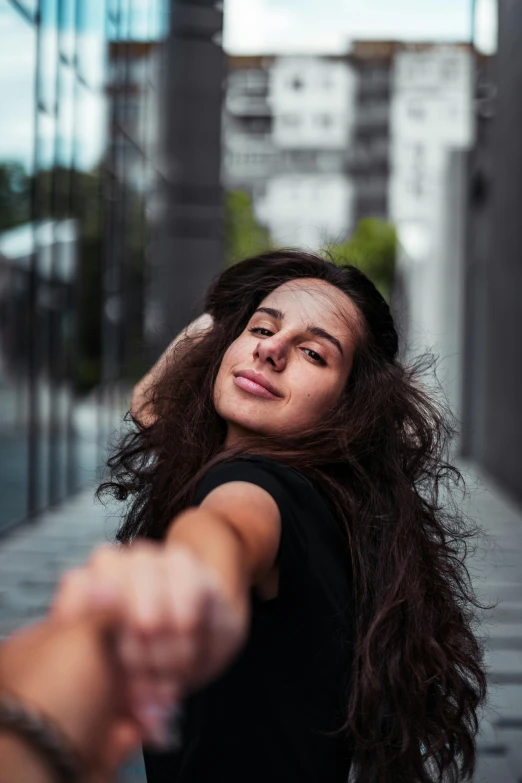 woman in black t - shirt holding her hand out near a building