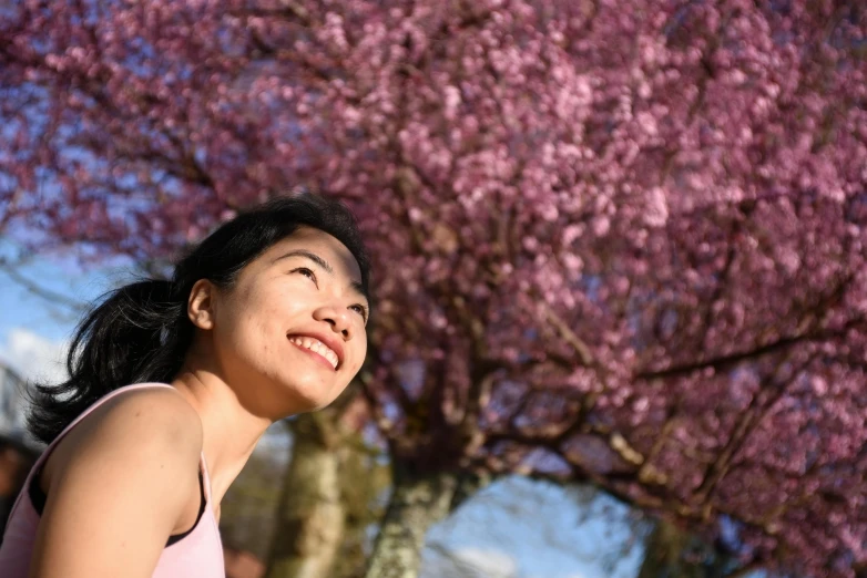 woman with black hair standing under a pink tree