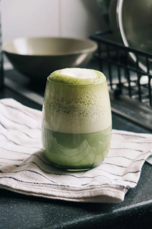 a green beverage with white liquid in it sitting on top of a towel