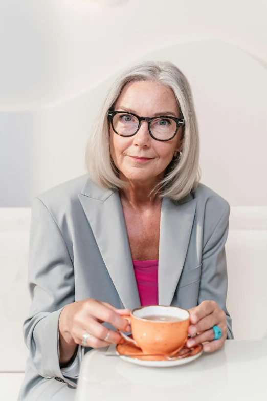 a woman with glasses sits at a table holding a cup