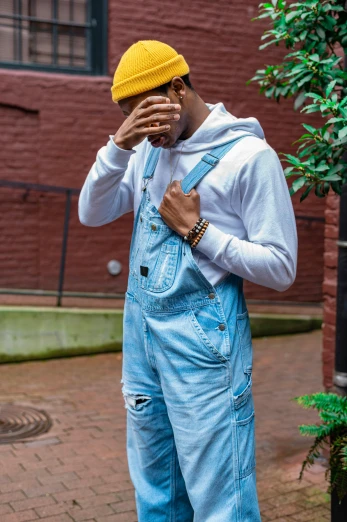 an african american man in overalls and a hat covers his face