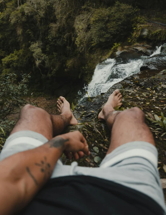 man laying next to waterfall with feet in the air