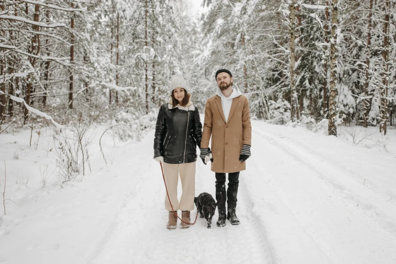 a man and woman holding hands walking their dog in the snow