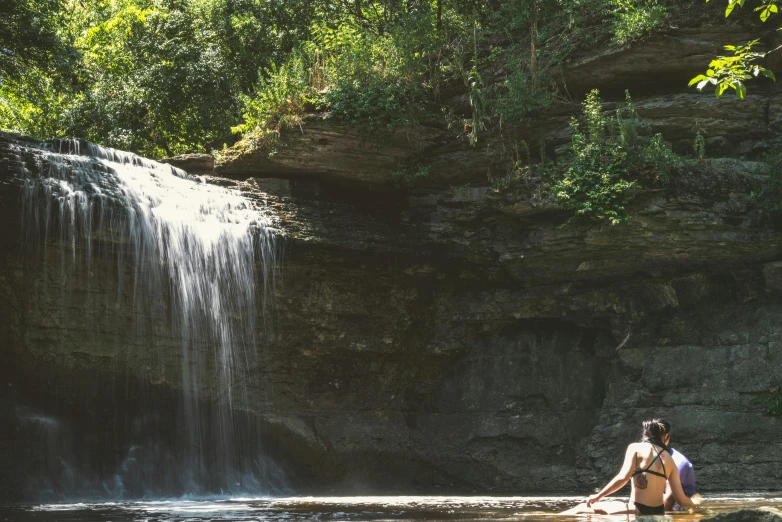 a woman standing in a river below a waterfall