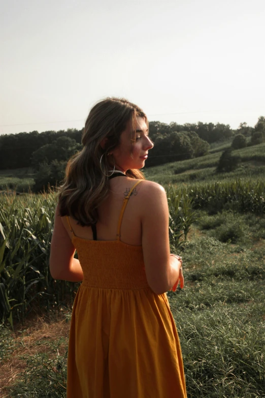 a girl in a yellow dress looks toward the horizon while holding her hands together