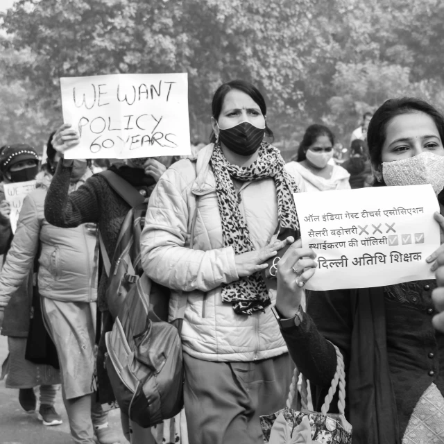 women with face masks protest in front of a crowd of men holding signs