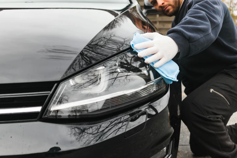 man cleaning the scratch on the front hood of a black car