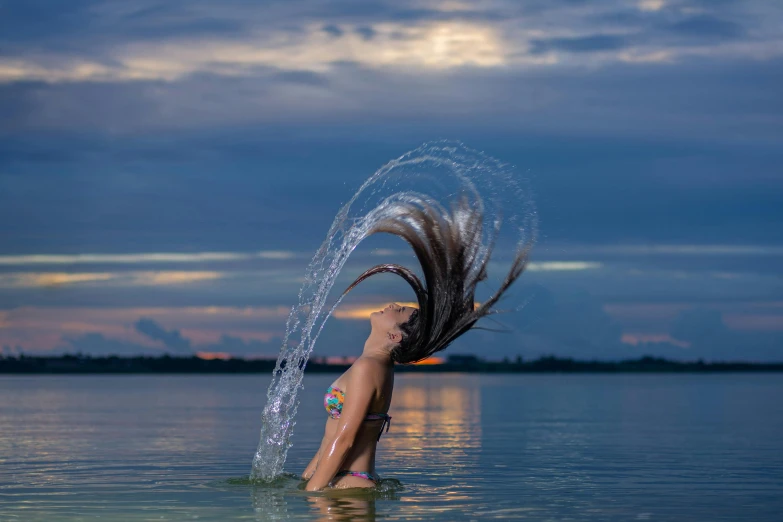 a girl is standing in the water throwing her hair in the air