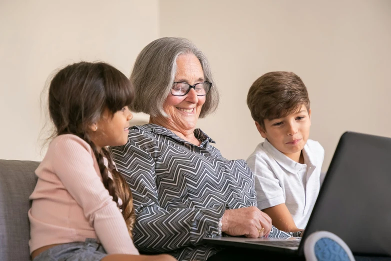 an old woman working on a laptop while two children watch