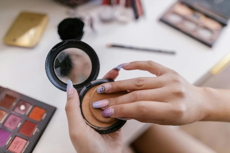 a hand holding a compact mirror in front of makeup and make up tools