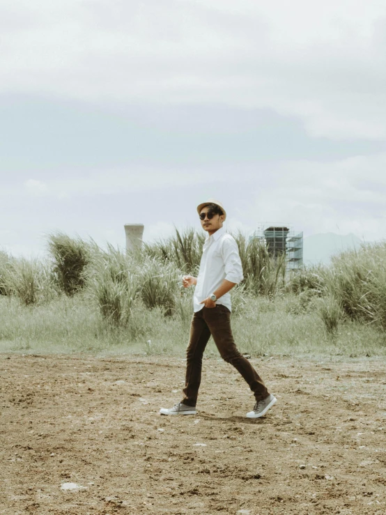 a man walking across a dirt field in front of a building