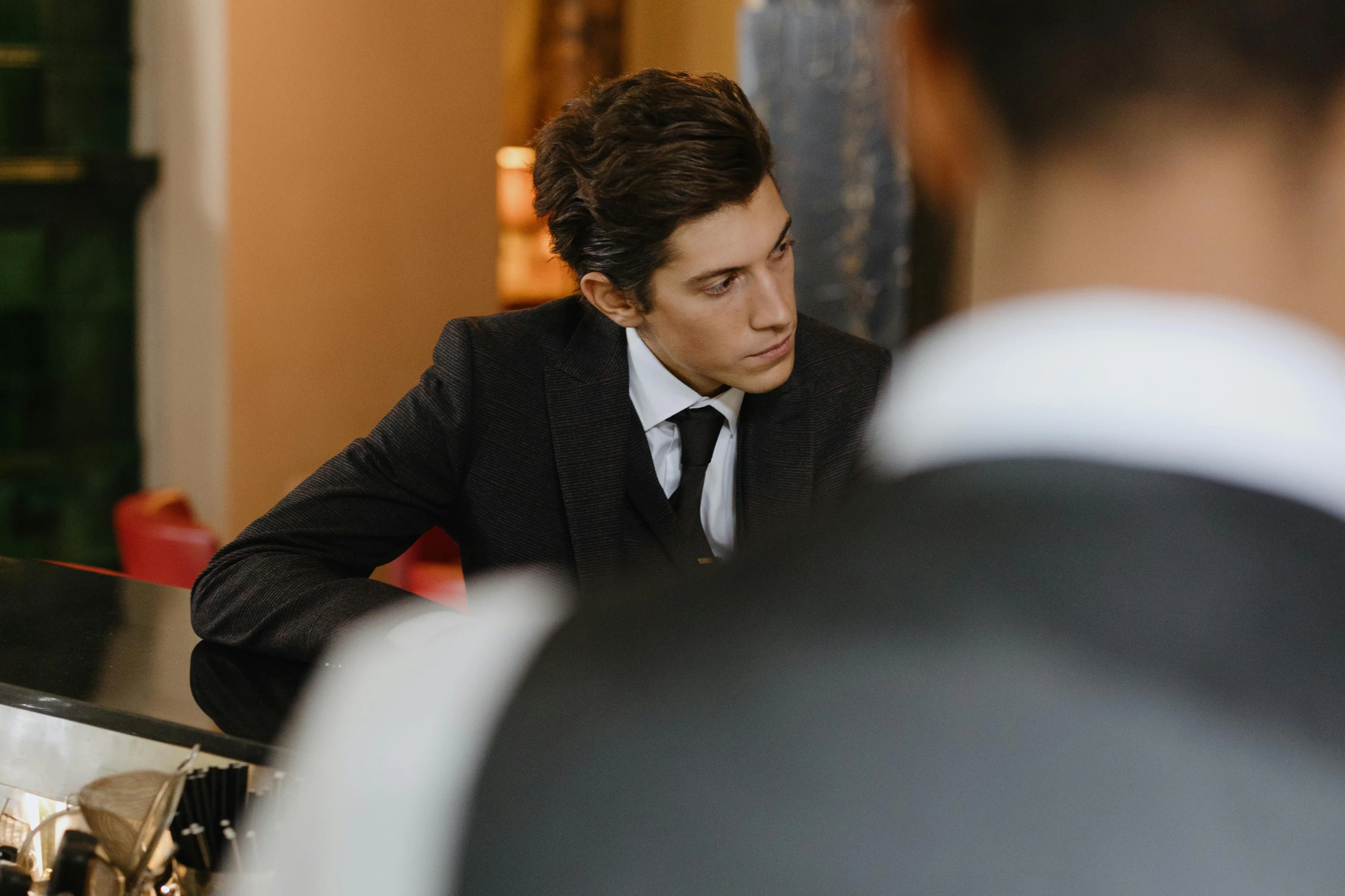 the young man is wearing a suit and sitting behind the counter