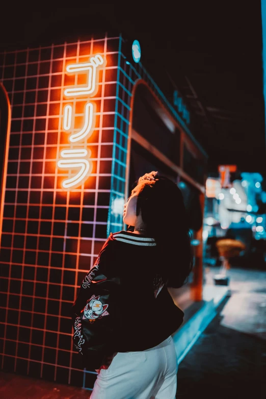 a woman standing on the side of the road looking up at a neon sign