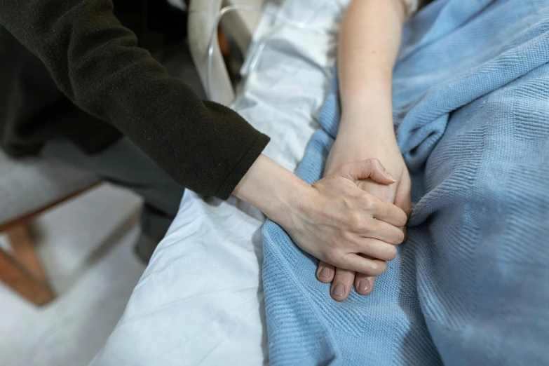 a woman holds the hand of a man sitting in bed