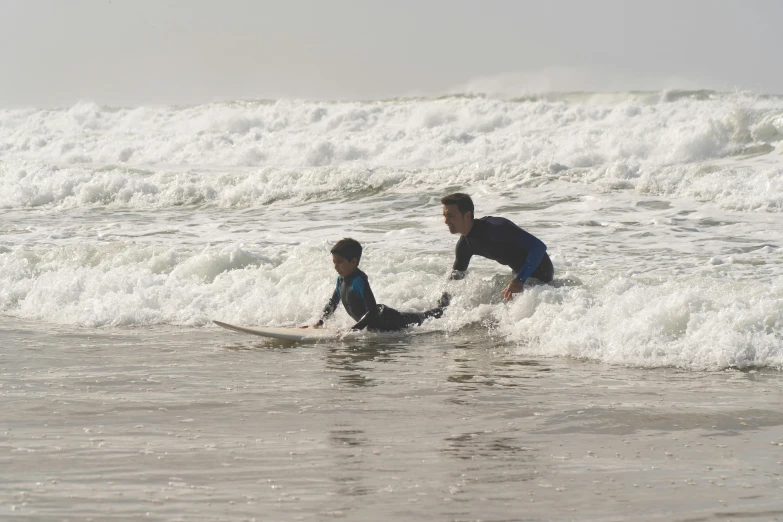 a man riding on top of a surfboard next to a small boy