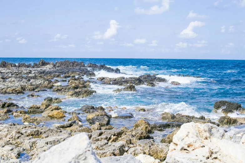 a rocky coast with the ocean and white clouds above it