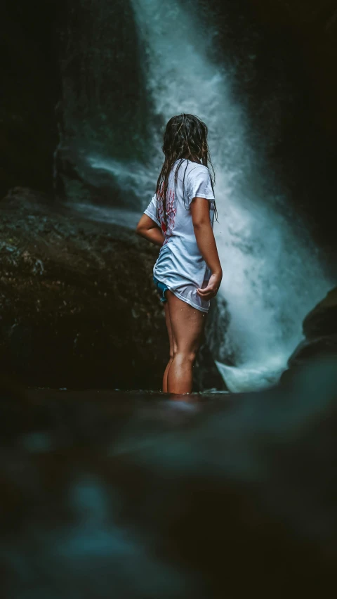 a woman standing next to a water fall in front of a forest