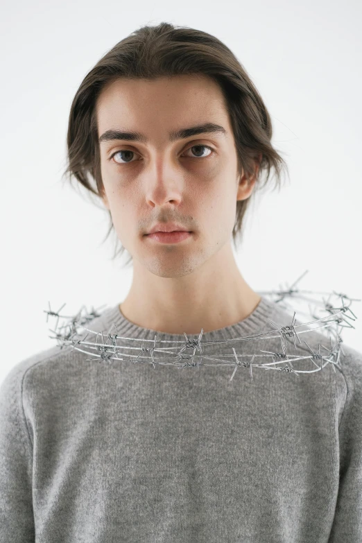 young man in gray sweater standing with barbed wire around his shoulders