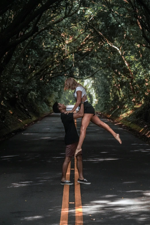 a man holding a woman in his lap while they are standing in the middle of a road