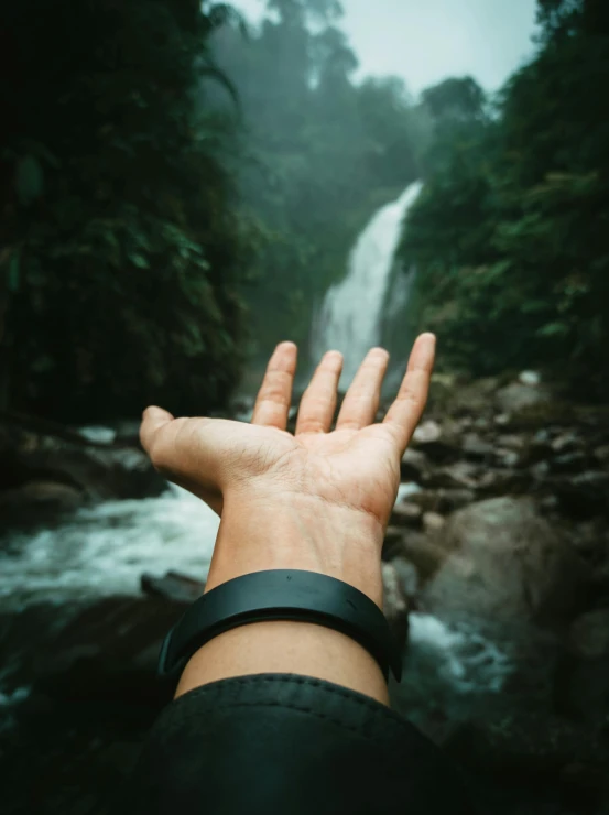 a person's hand reaches towards a waterfall