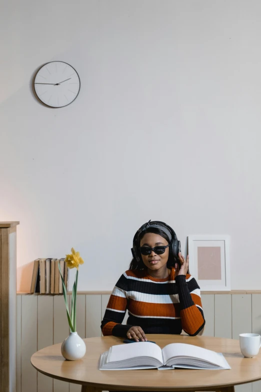 a young person wearing glasses holding a phone over an open book on a wooden table