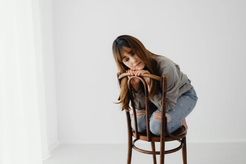 a woman sitting on a wooden chair leaning on her head