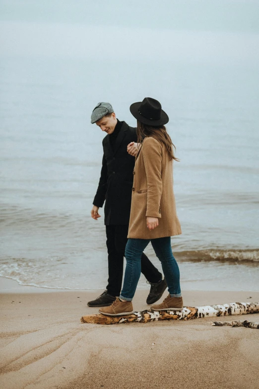 a young woman and man walking on the beach next to the ocean