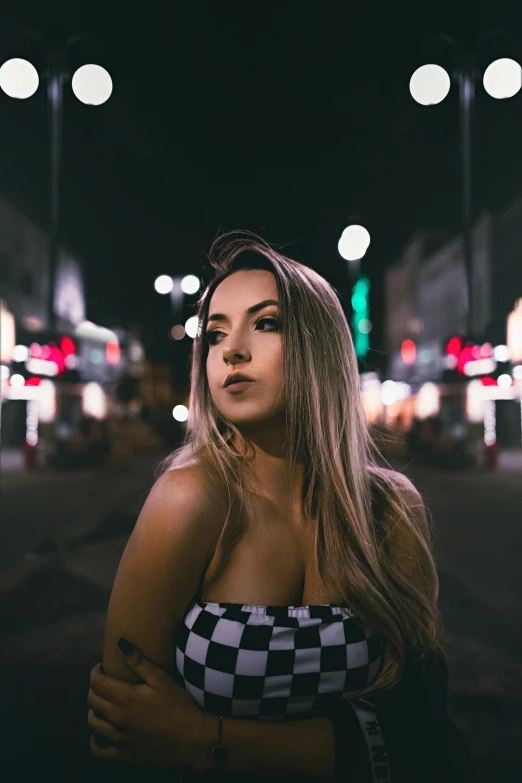 a woman standing outside at night wearing a checkered top