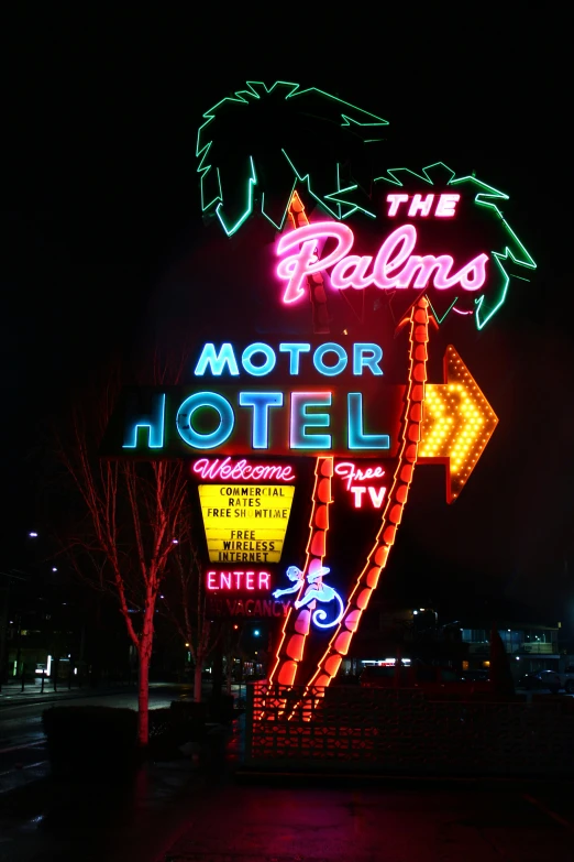 a brightly lit motel sign sitting next to a tree