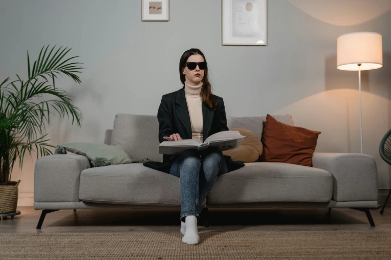 a woman sitting on top of a couch while reading a magazine