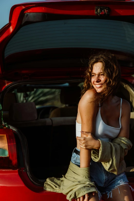 a woman sitting on the back of a red car