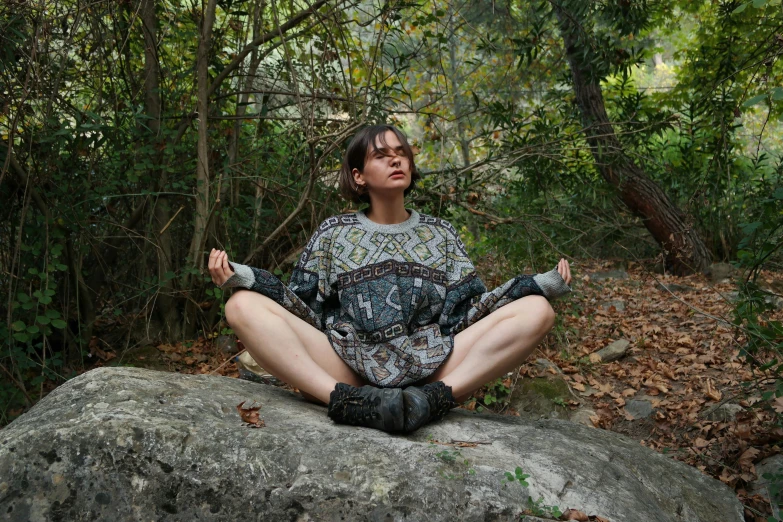 a woman sits on top of a rock and practices meditation
