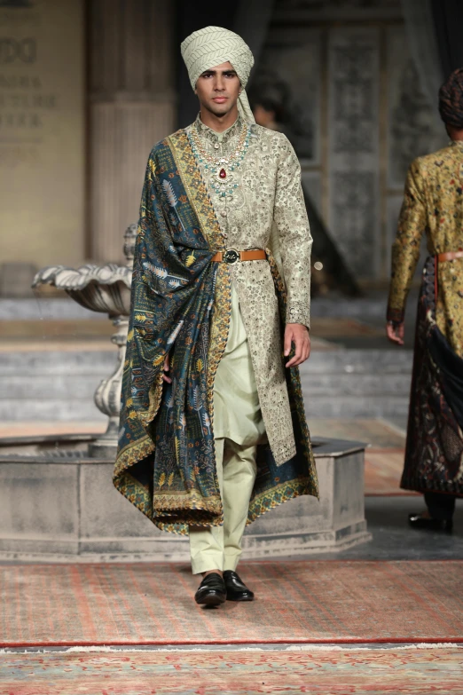 a man wearing an elaborately designed outfit and turban on the runway