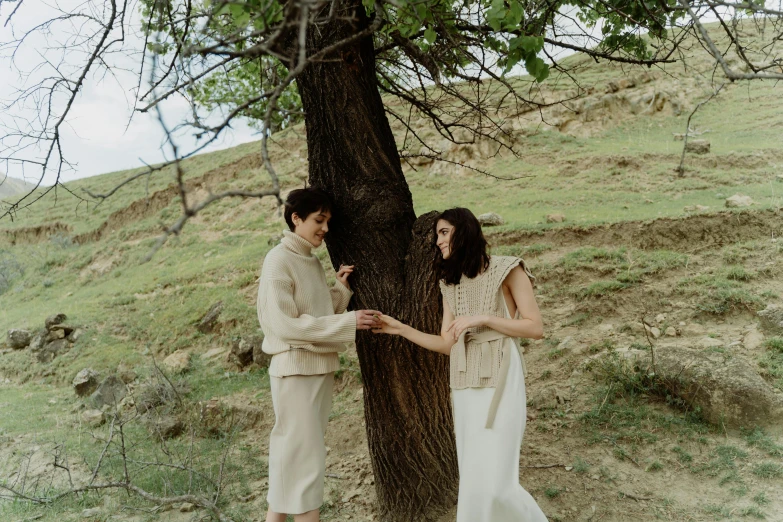 a couple standing next to a tree holding hands