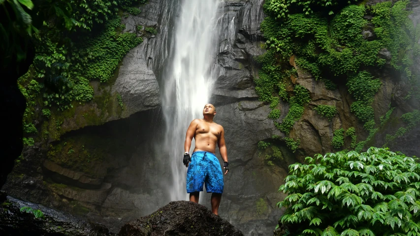 a shirtless man standing at the base of a waterfall