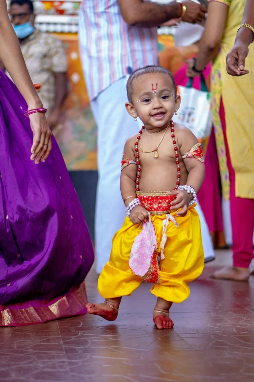 a little girl in yellow and purple is walking towards a group of people