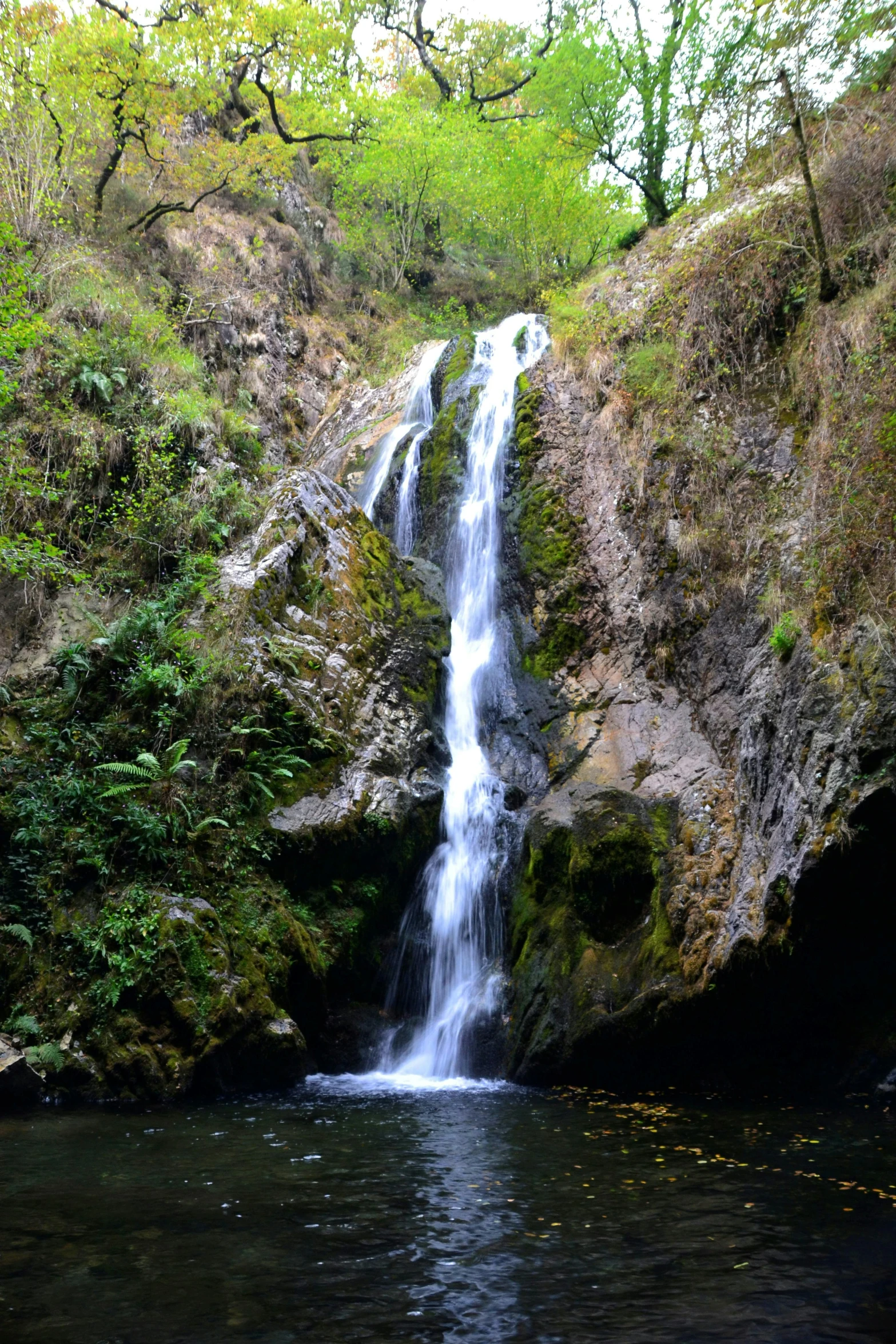 a waterfall cascading over a river under a lush green hillside