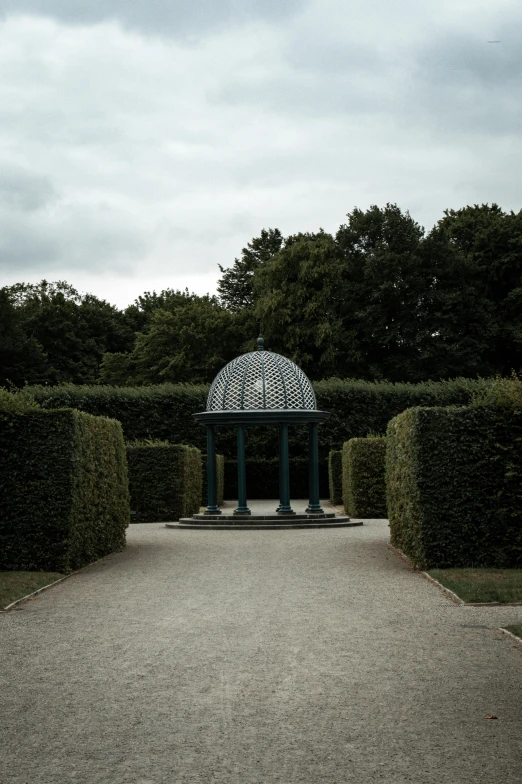 a well - kept garden with trimmed hedges and an ornamental iron gazebo