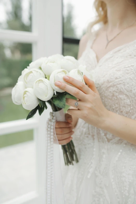 a woman in white dress holding flowers near a window