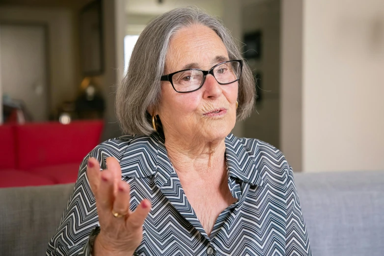 an old woman wearing glasses, talking to someone