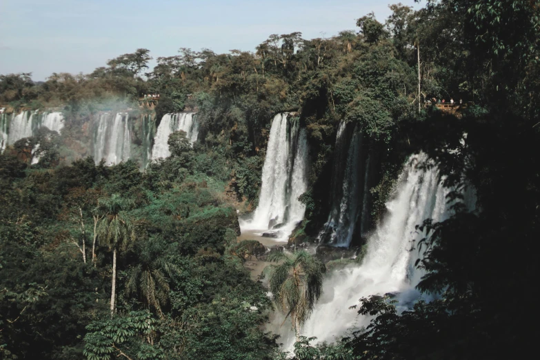 a lush green hillside with several tall waterfalls in the background